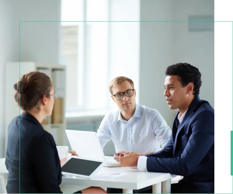 Three people sitting at a table with one of them holding a laptop.